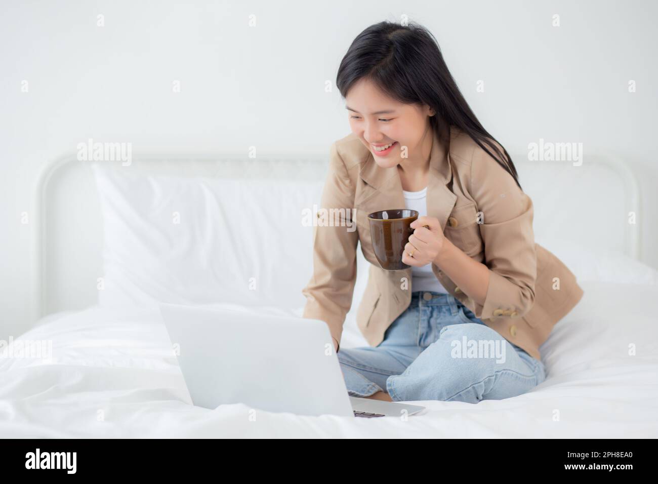 Beautiful young asian woman sitting on bed using laptop computer ...