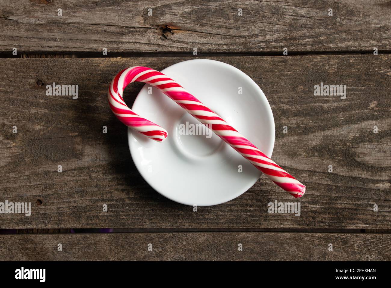 New Year's caramel in the form of a cane in red and white stripes lies on a plate on the table, New Year's decor Stock Photo