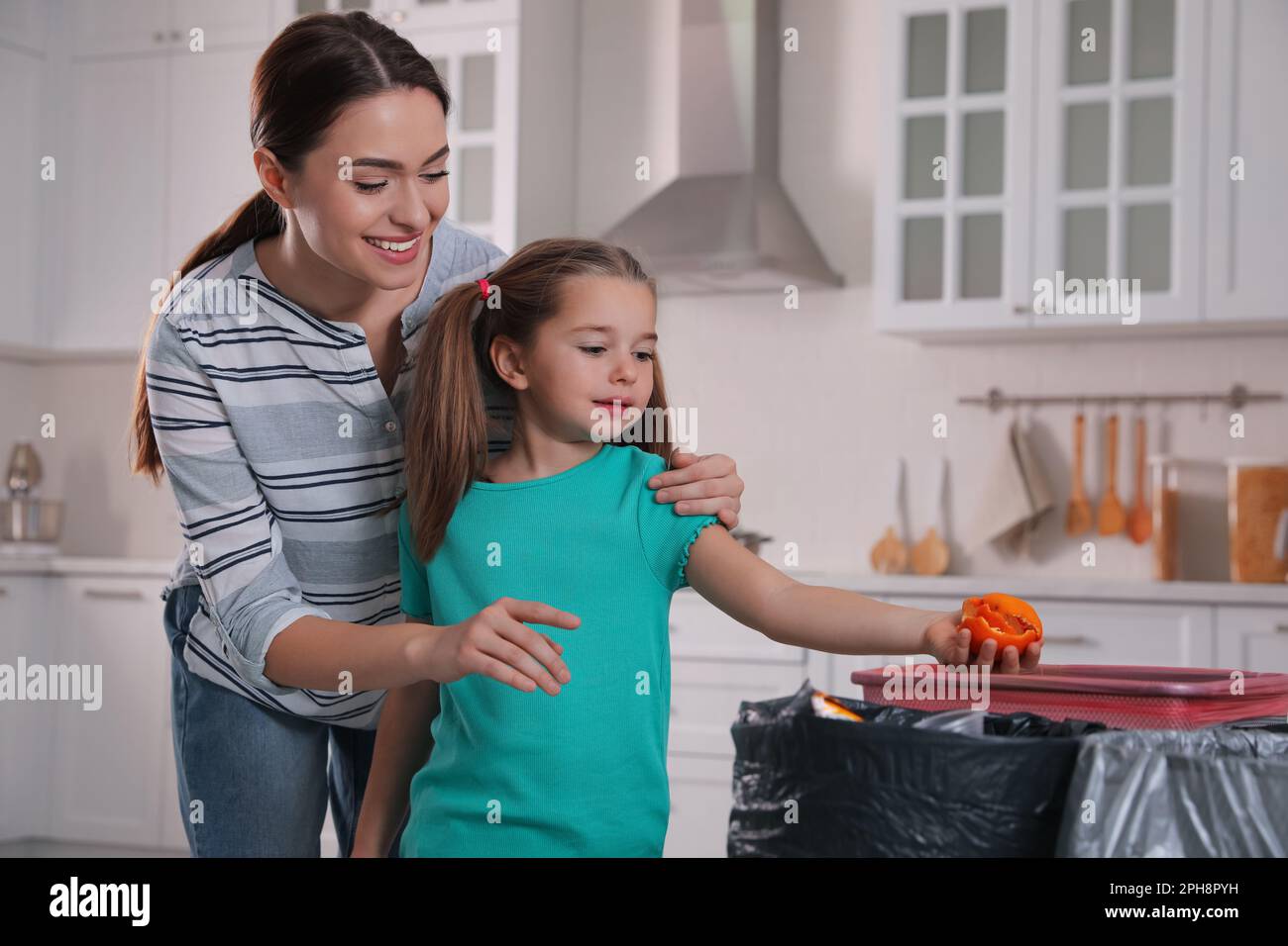 Little girl throwing tangerine peel into trash bin in kitchen. Separate waste collection Stock Photo