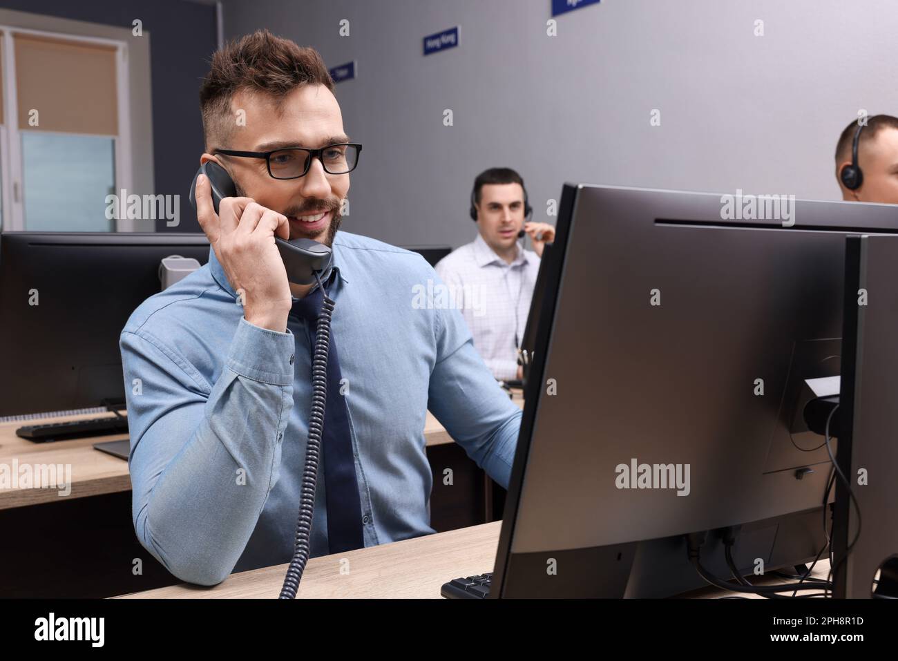 Handsome call center operator talking on phone and his colleagues ...