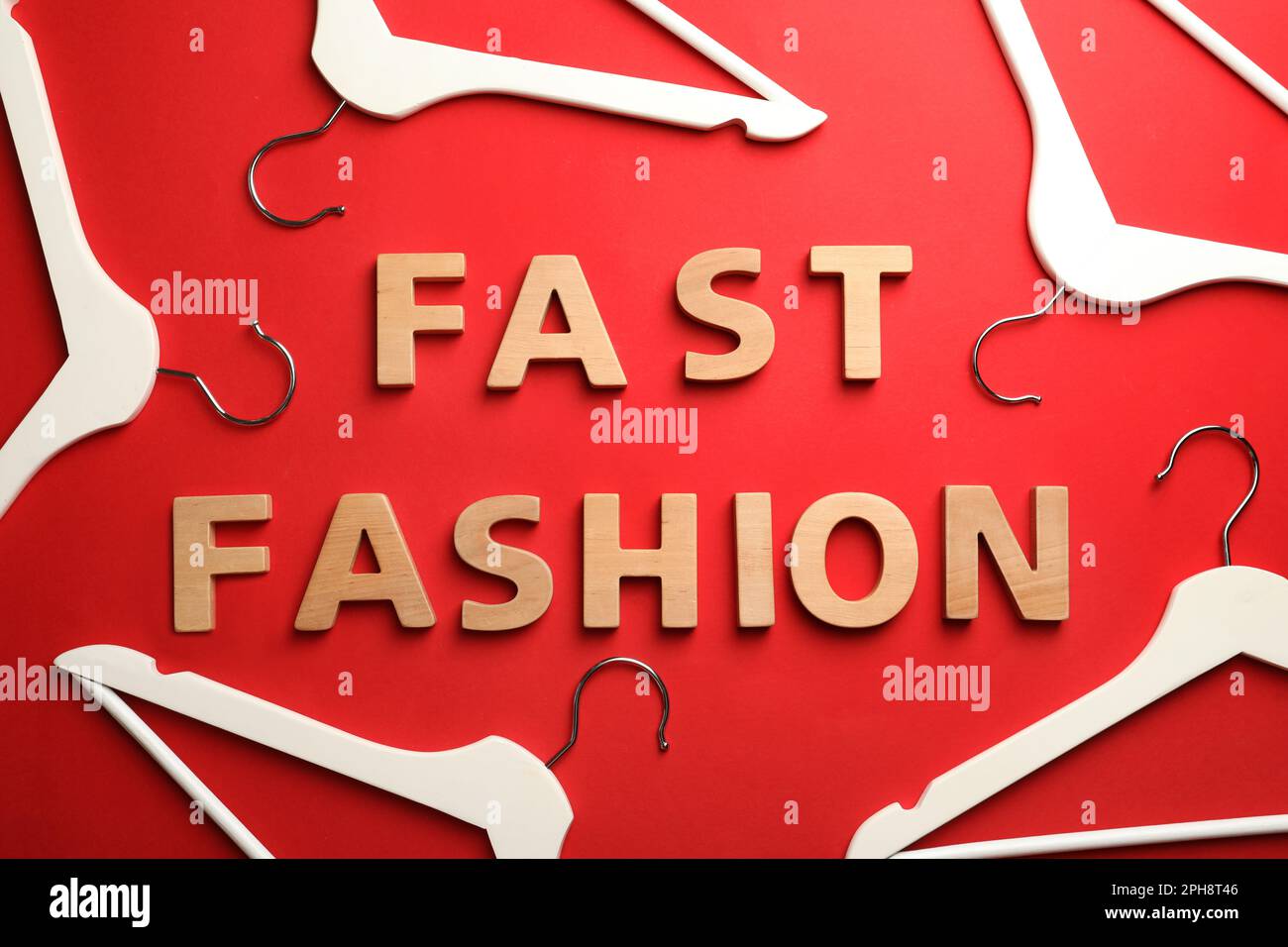 Phrase FAST FASHION made of wooden letters and white hangers on red background, flat lay Stock Photo