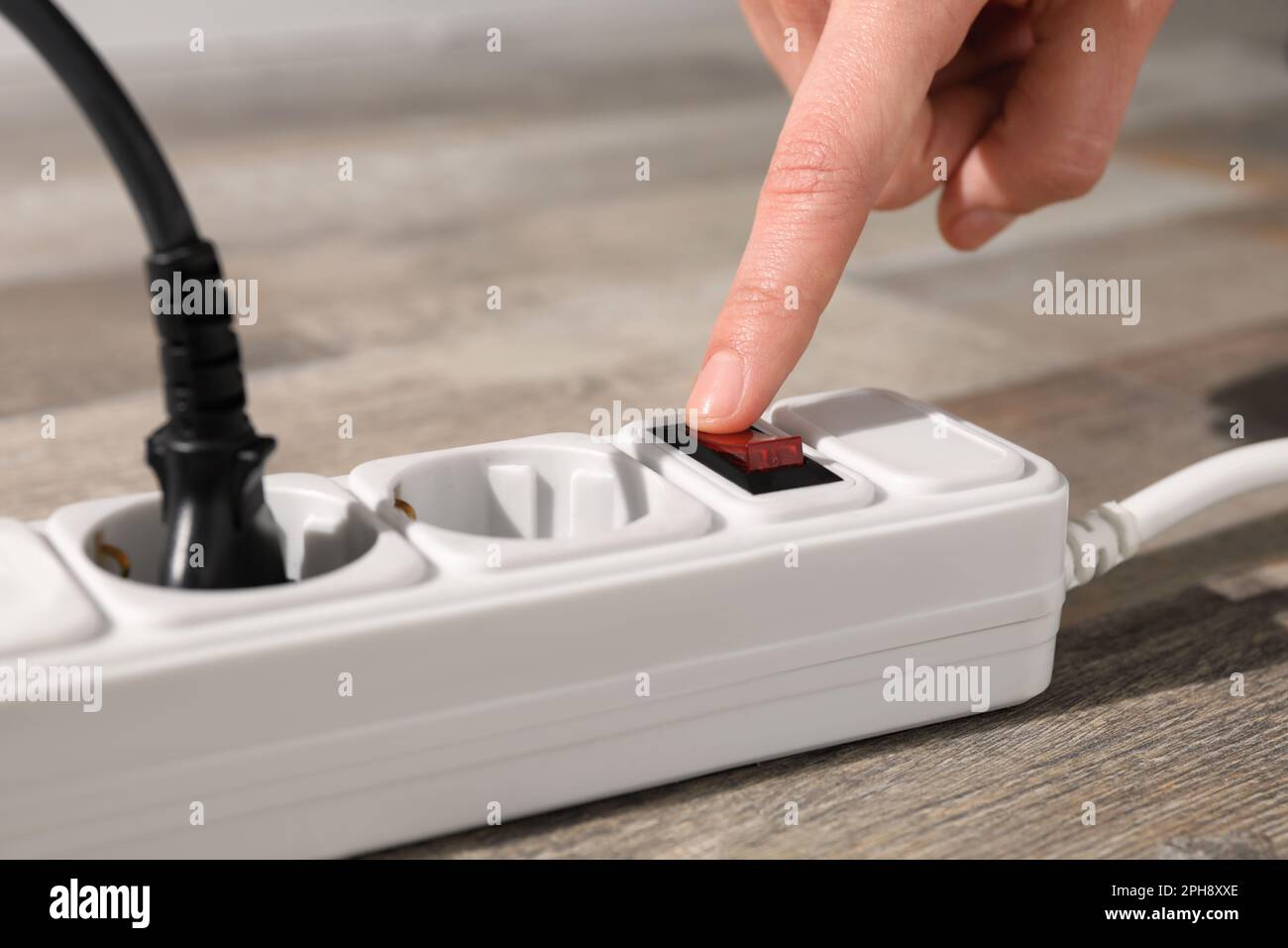 Man pressing power button of extension board on floor, closeup Stock