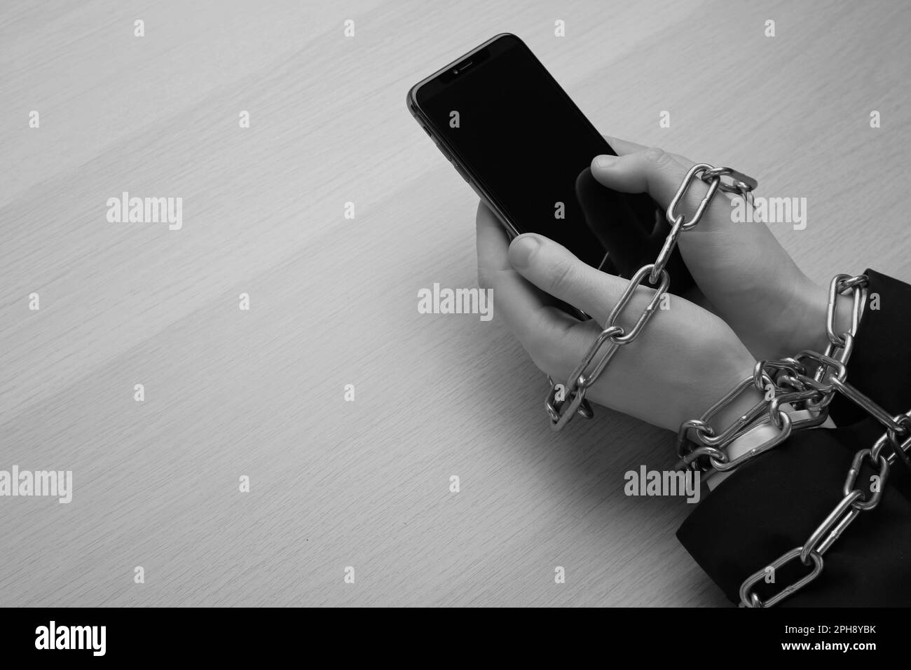 Above view of internet addicted woman with chained hands using smartphone at wooden table, space for text. Black and white effect Stock Photo