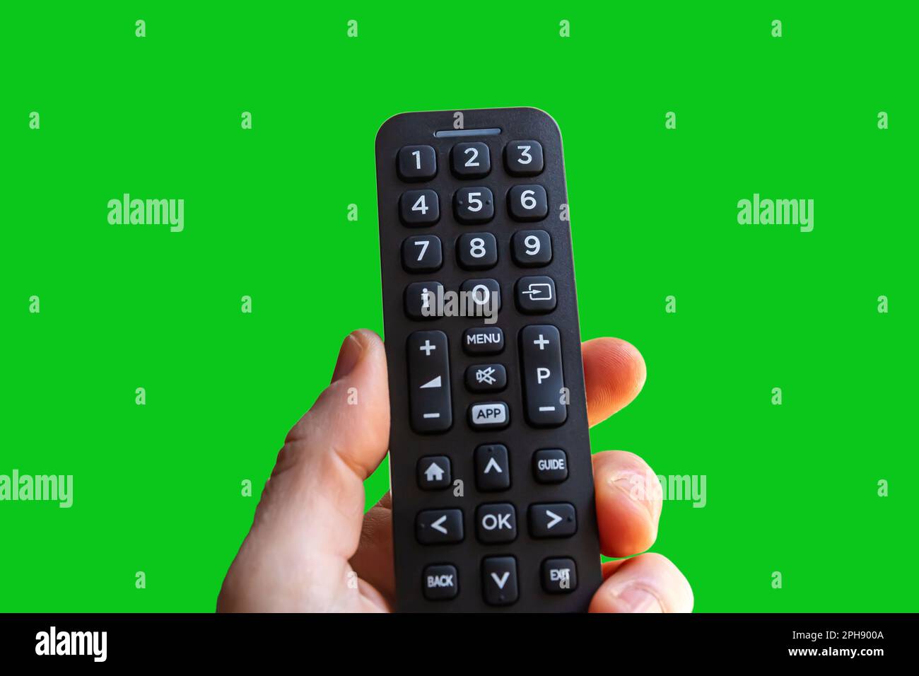 A man is holding a remote control of a smart TV in his hand on a green