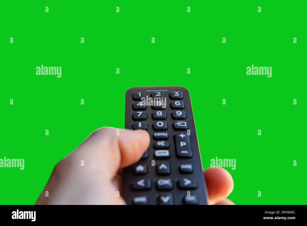 A man is holding a remote control of a smart TV in his hand on a green