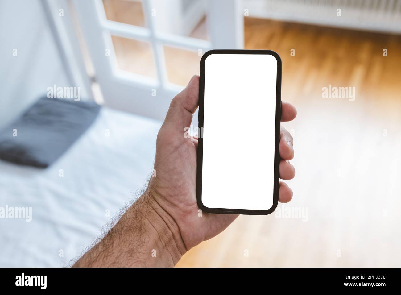 Man holding smart phone device with blank mockup screen in bedroom. Copy space for app or text message. Stock Photo