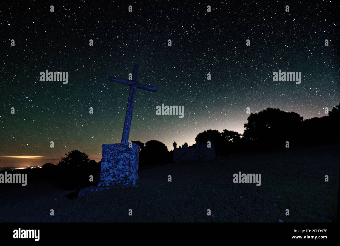 Long Exposure night photograph with stars in the background and foreground a cross and trees Stock Photo