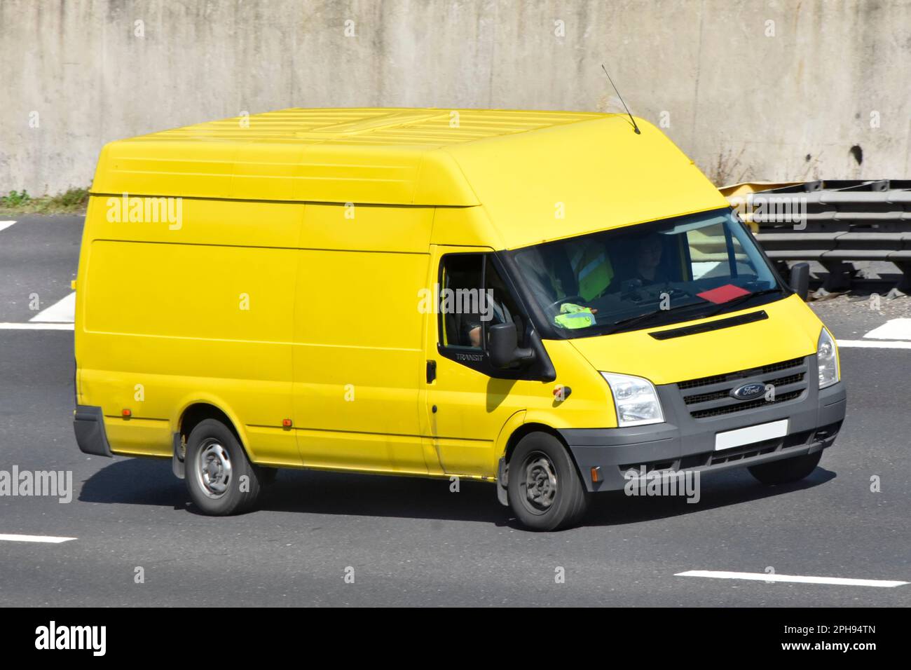 Commercial vehicle driver in side and front view of clean unmarked  yellow Ford Transit high roof van driving along M25 motorway road Essex England UK Stock Photo
