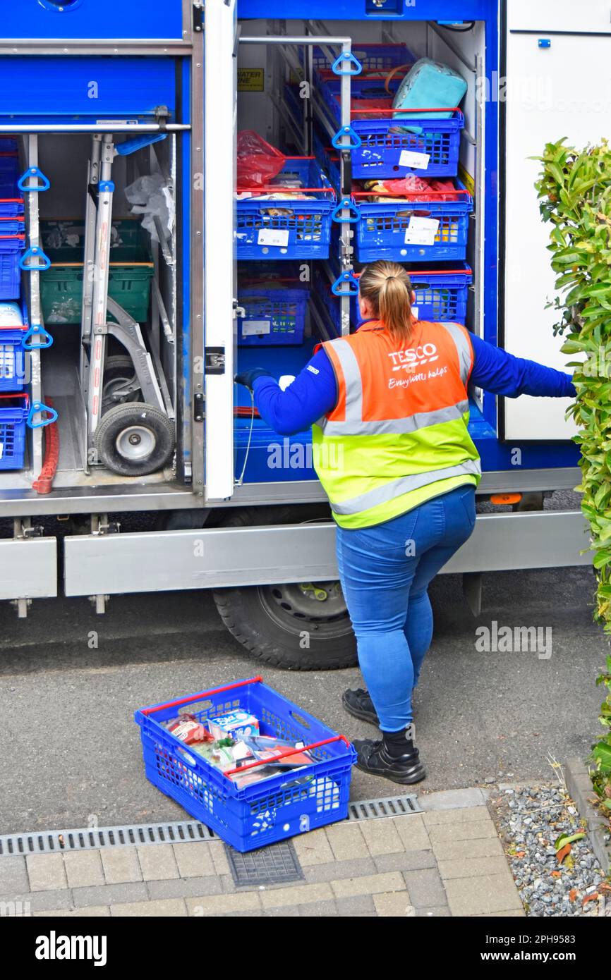 Tesco Supermarket close up home internet grocery shopping delivery  blue crates unloaded by woman van driver wearing high visibility jacket England UK Stock Photo