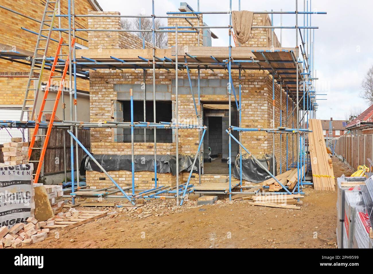 New build infill detached residential property with superstructure brick walls progressing beside flank wall of adjoining neighbour house England UK Stock Photo