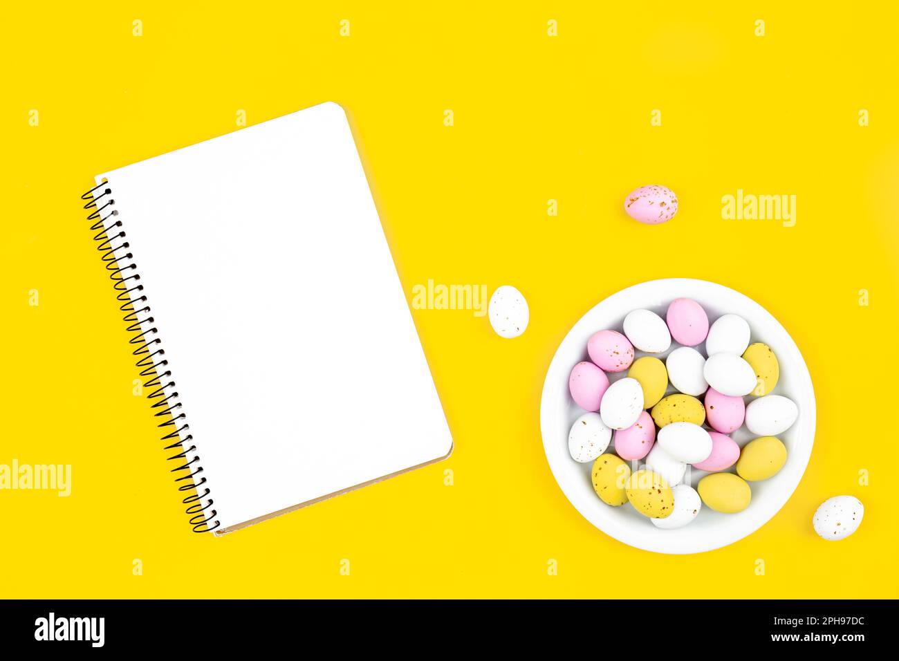 Colored Easter eggs and a blank notepad on a yellow background. Stock Photo