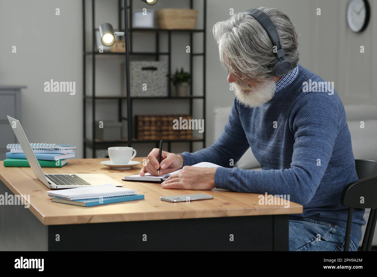 Man Computer Learing Middle aged man with laptop, notebook and headphones learning at table ...