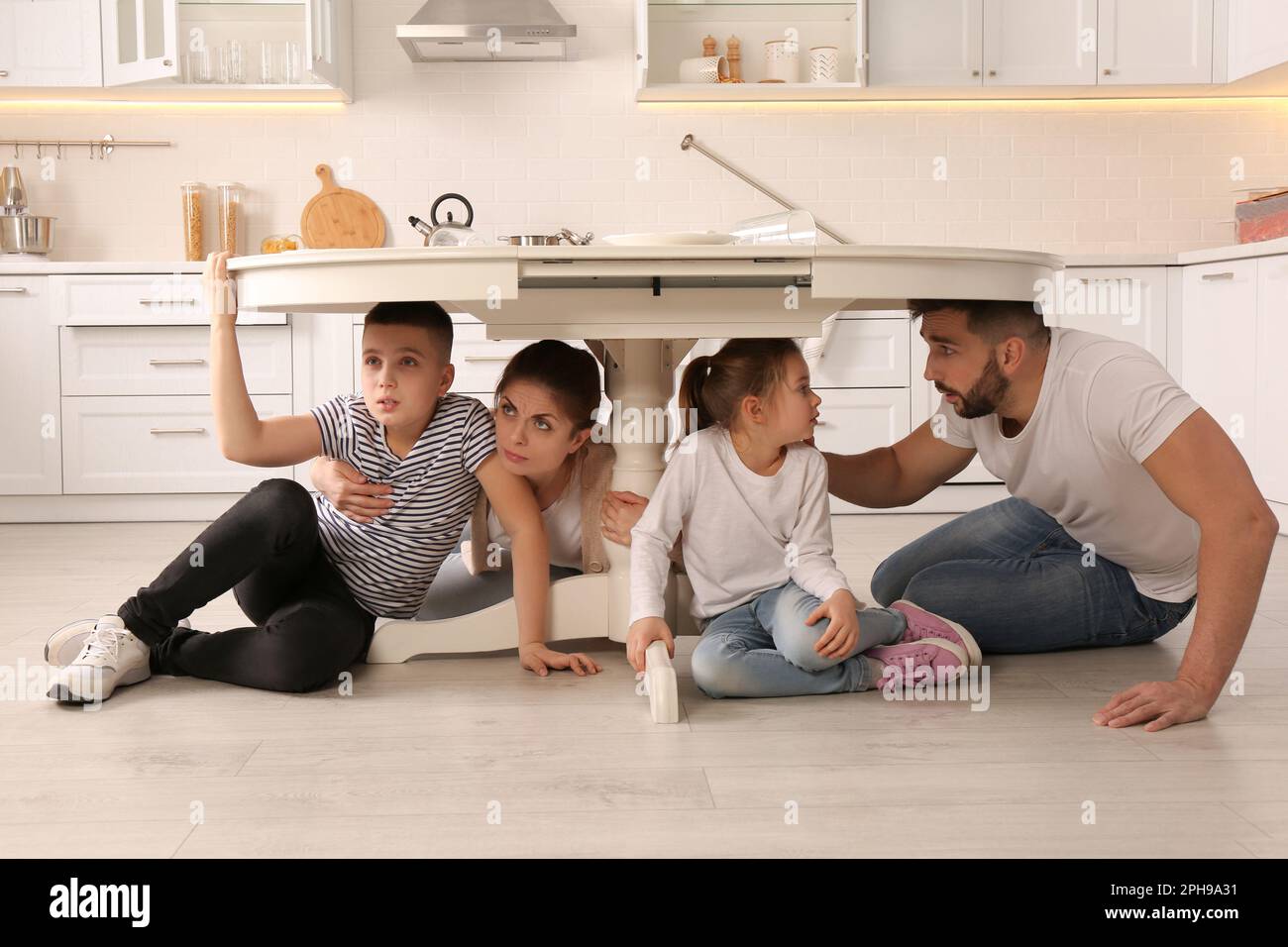 Scared parents with their children hiding under table in kitchen during