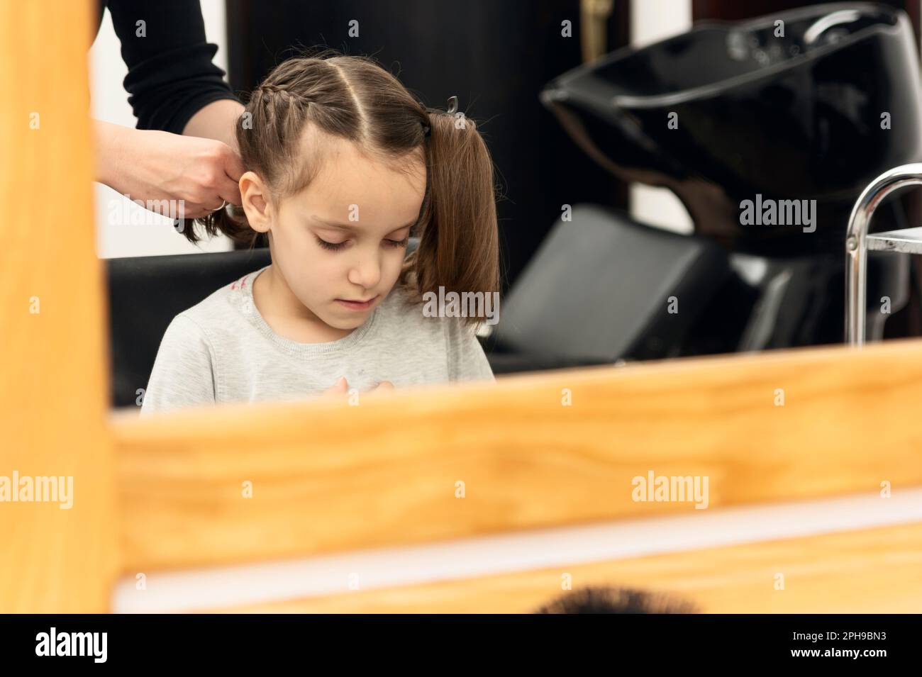 Hairdresser makes braids for small girl in hair salon Stock Photo Alamy