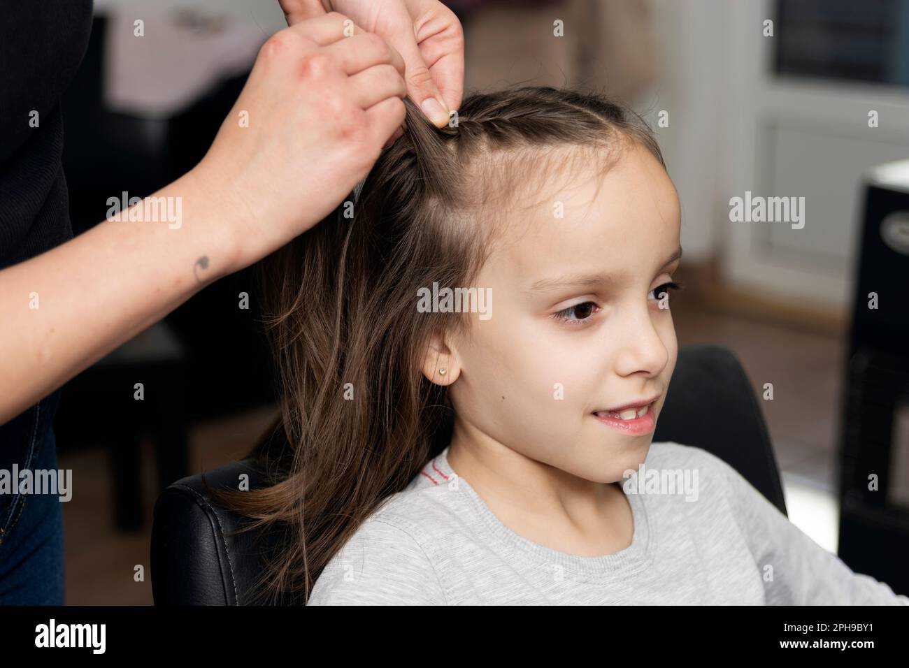 Hairdresser makes braids for small girl in hair salon Stock Photo Alamy