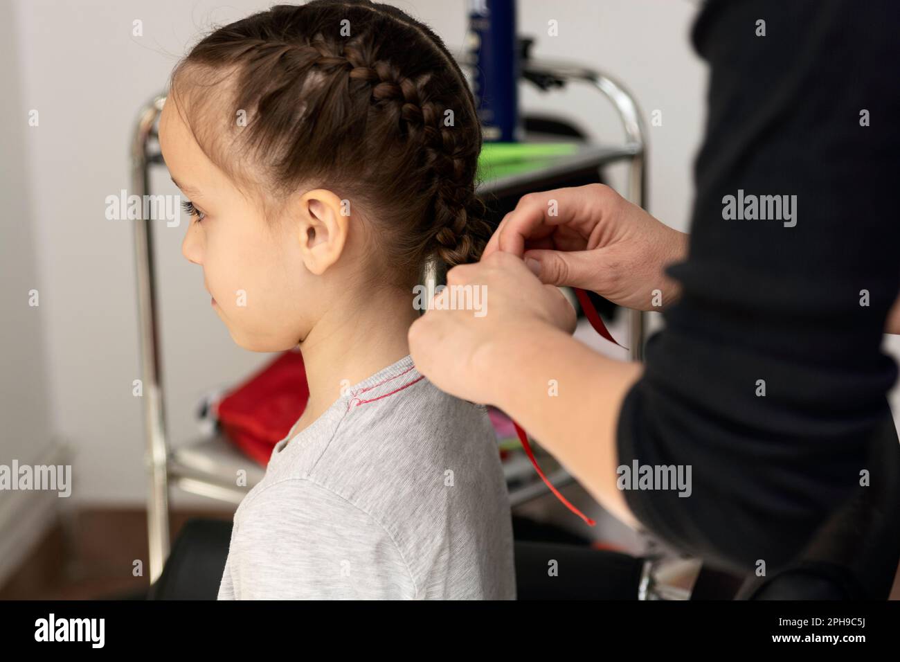 Hairdresser makes braids for small girl in hair salon Stock Photo Alamy