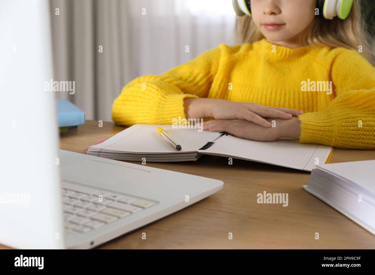 Cute little girl with modern laptop studying online at home, closeup. E ...