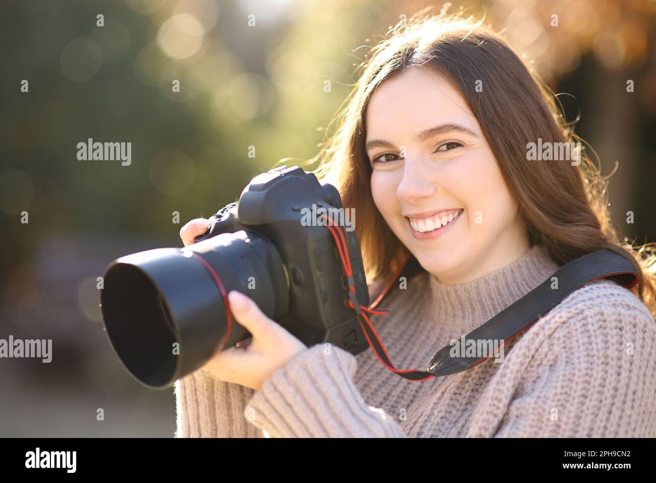 Happy photographer holding dslr camera looks at you in a park Stock Photo