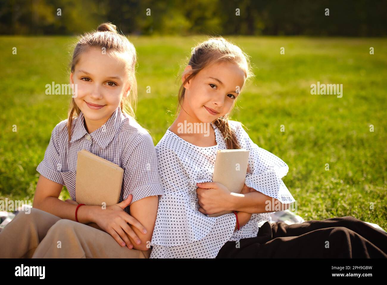 Portrait Of Two Happy Girls Sisters Reading In Green Park Girls Hold