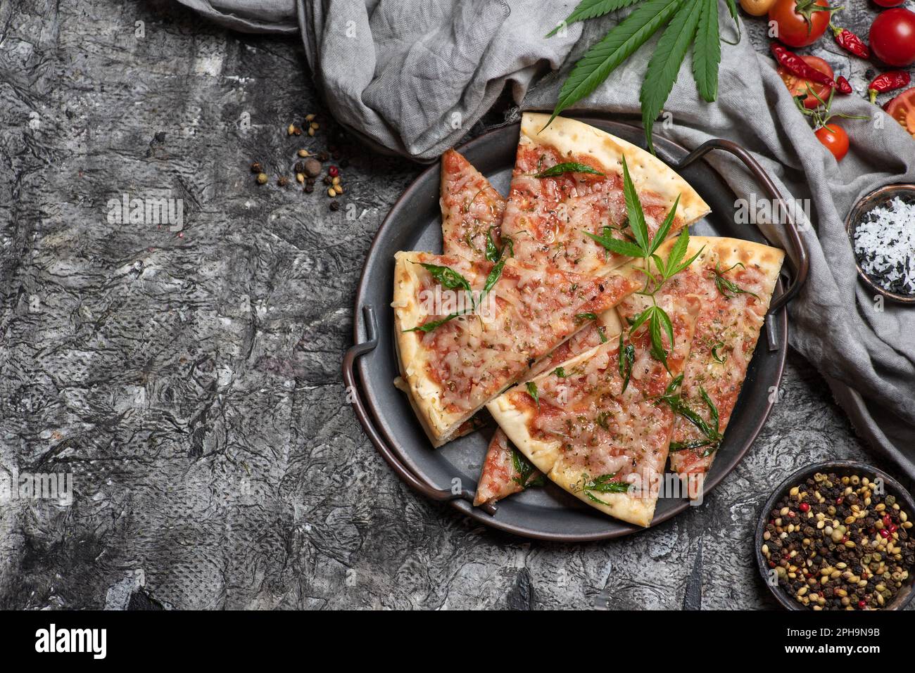 Pizza slices with marijuana leaves in a metal bowl on a dark wooden background Stock Photo