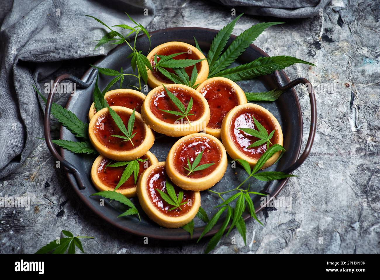 Biscuit with strawberry jam and marijuana leaf in a black bowl on a table top view Stock Photo