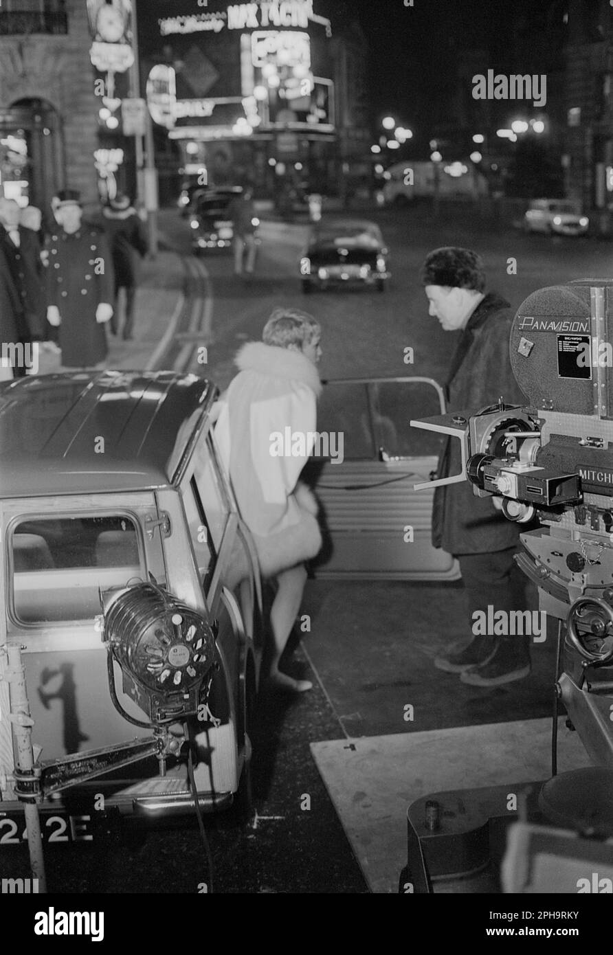 London. circa.1967. A photograph of Mia Farrow stepping out of an Austin Mini Countryman estate car whilst talking to the film director, Anthony Mann. Taken outside the Café Royal, Regent Street in Piccadilly, London, behind the scenes during the filming of the neo-noir British spy movie, ‘A Dandy in Aspic’. Stock Photo