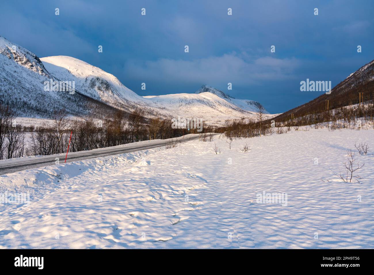 Morgenstimmung auf der Insel Senja und Kvaløya im Winter in Norwegen. Das Morgenrot färbt schneebedeckte Berge und Wolken rötlich, buntes Haus am Ufer Stock Photo