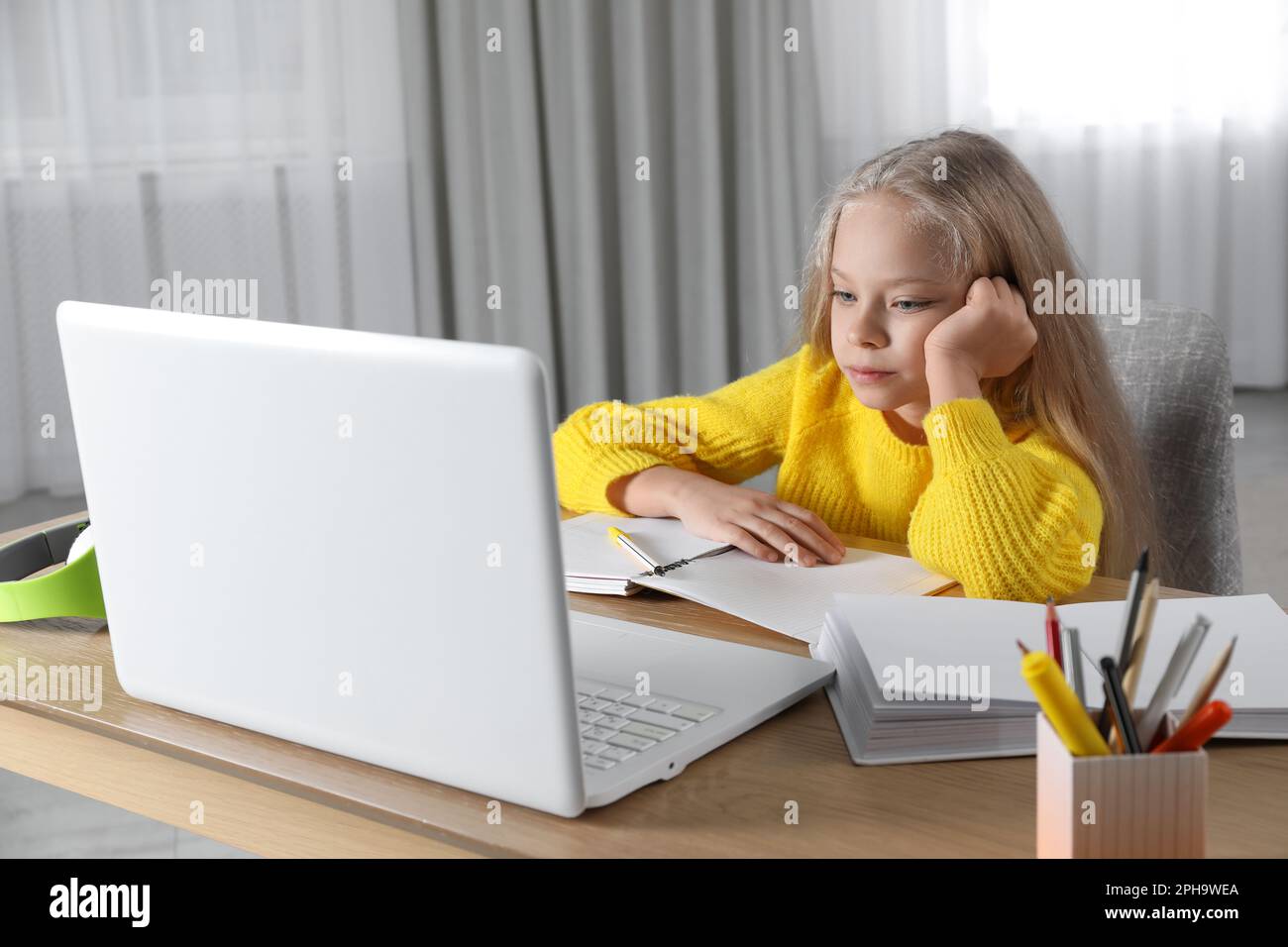 Cute little girl with modern laptop studying online at home. E-learning ...