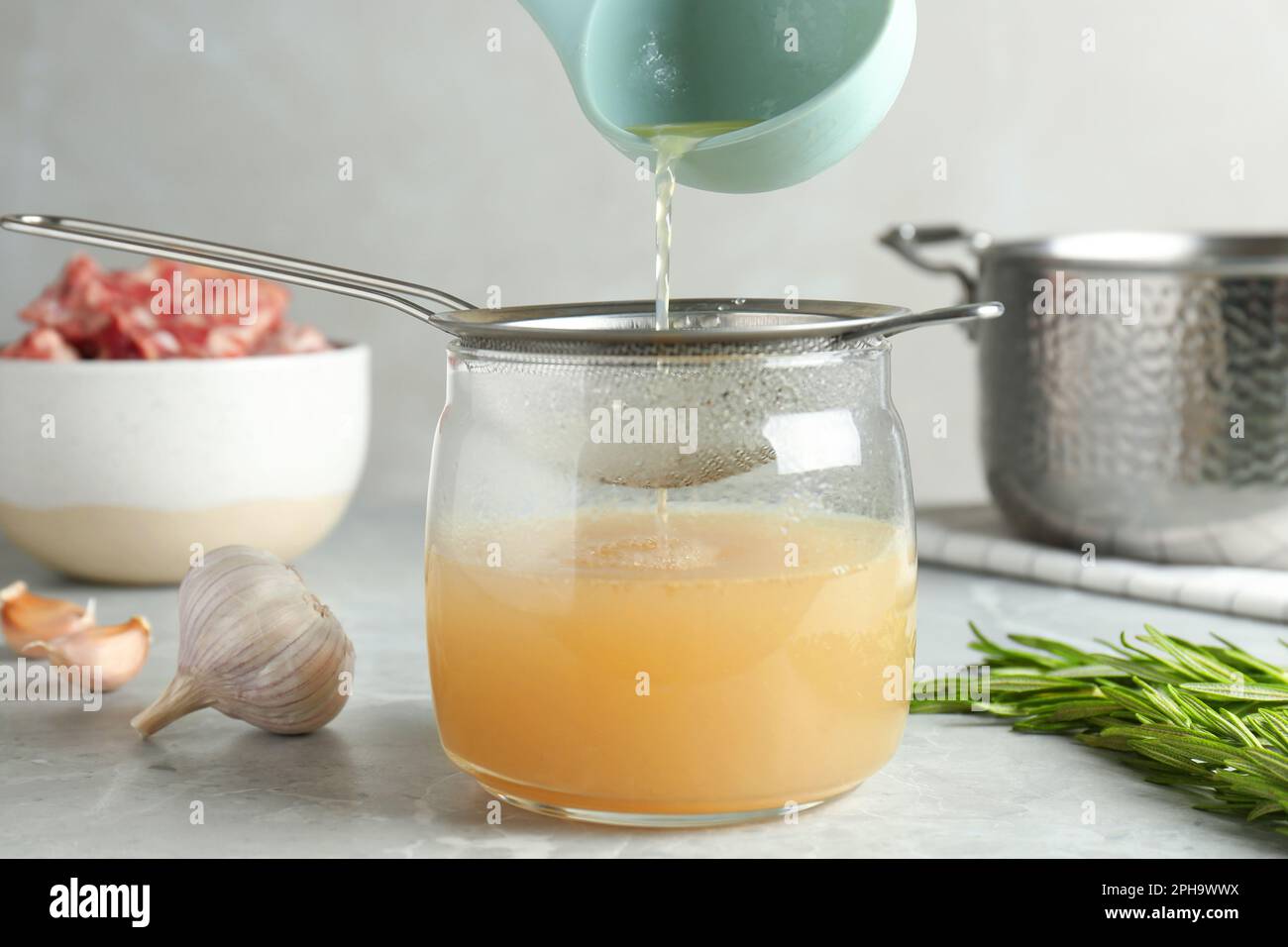 https://c8.alamy.com/comp/2PH9WWX/sieving-delicious-bone-broth-into-glass-jar-on-light-grey-table-2PH9WWX.jpg