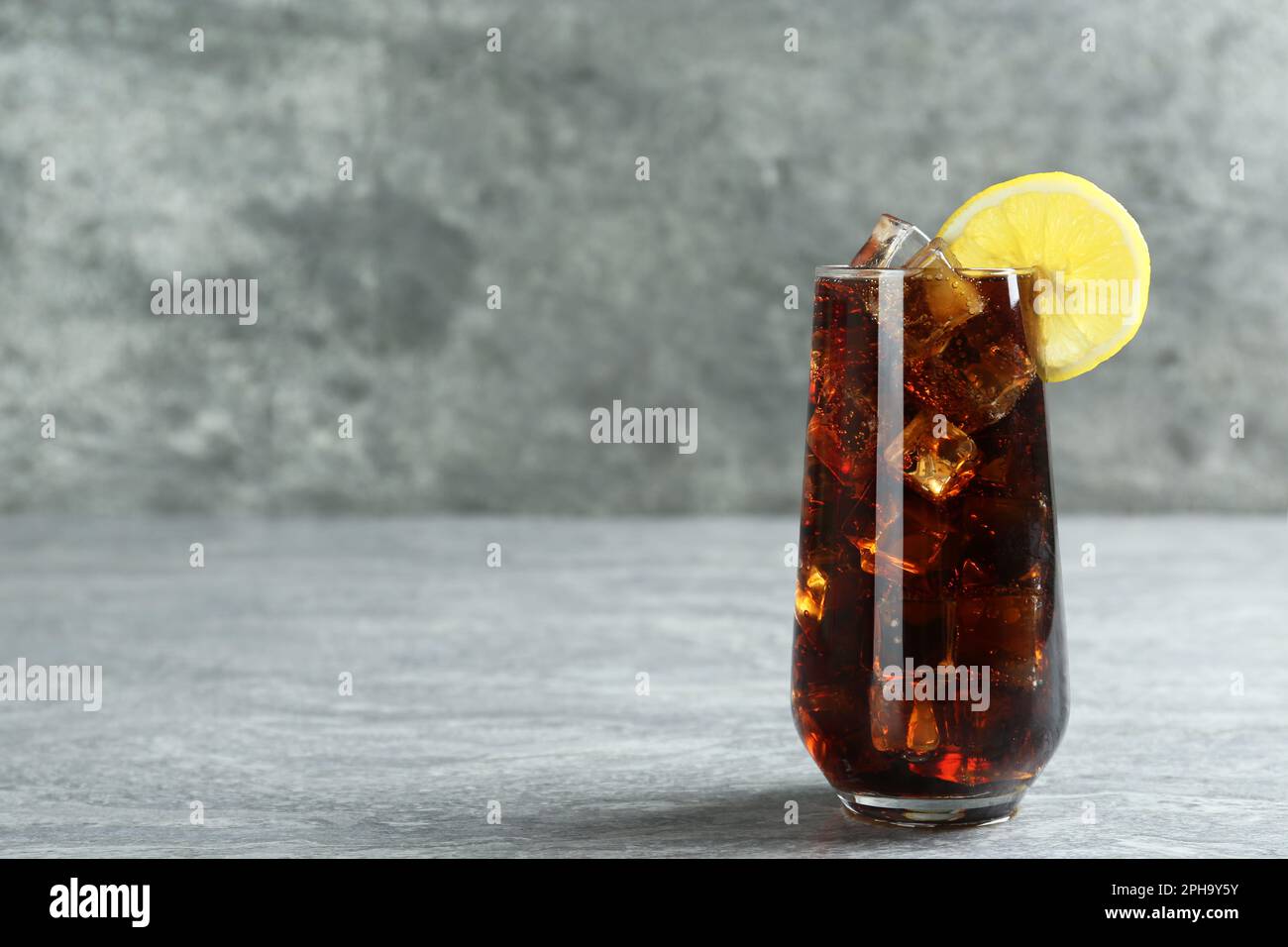 Glass of refreshing soda water with ice cubes and lemon slice on grey ...