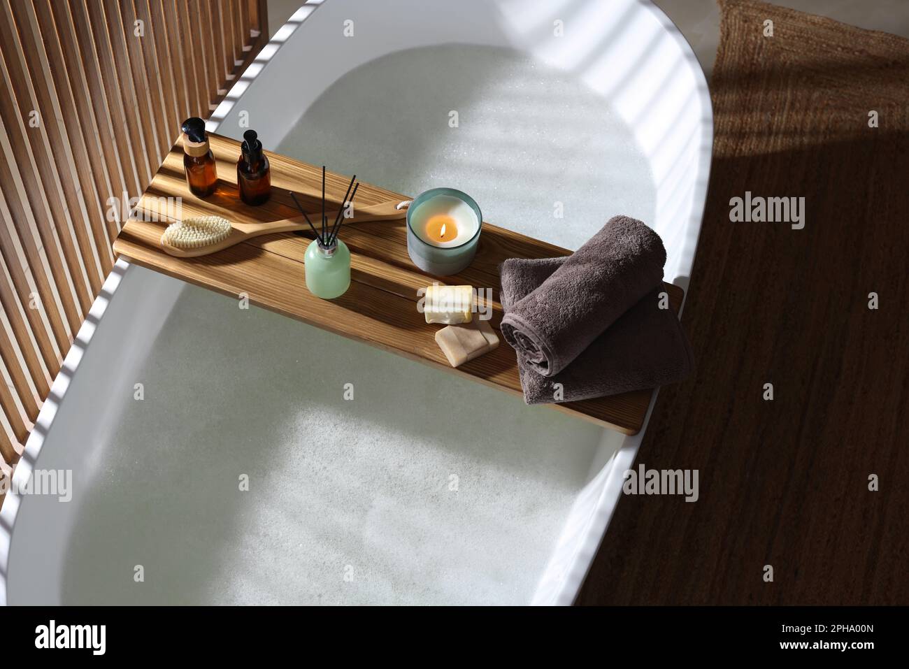 Wooden bath tray with candle, air freshener and bathroom amenities on