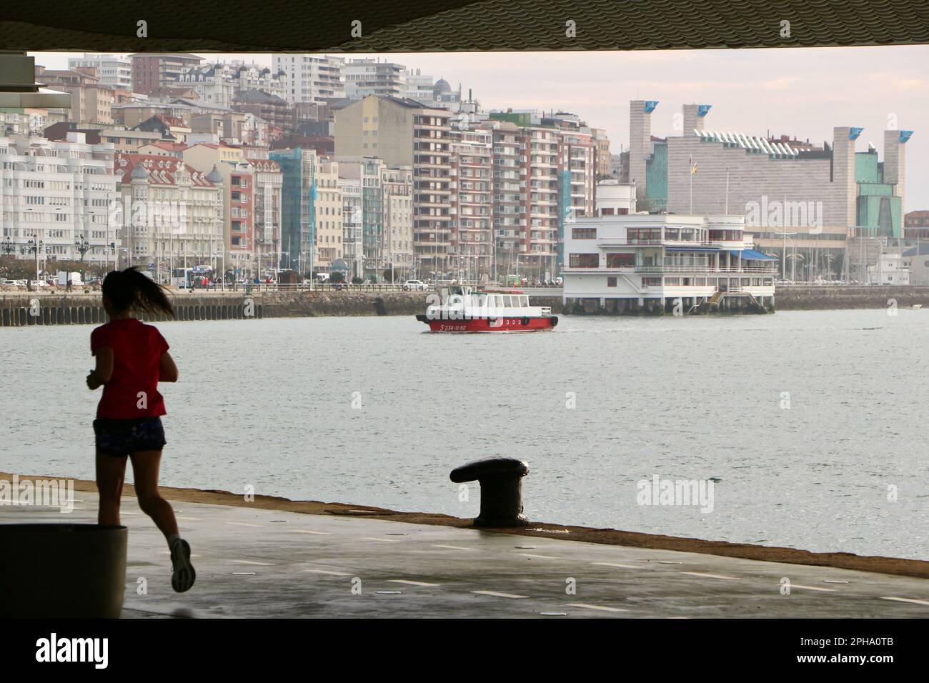 Female jogger passing under the Botin Centre Santander Cantabria Spain with a Regina ferry the Royal Yacht Club and Festival Palace in the distance Stock Photo