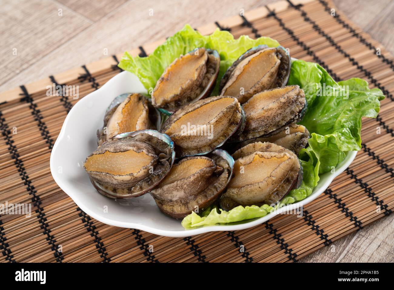 Delicious raw abalone in a plate with lettuce on wooden table background. Stock Photo