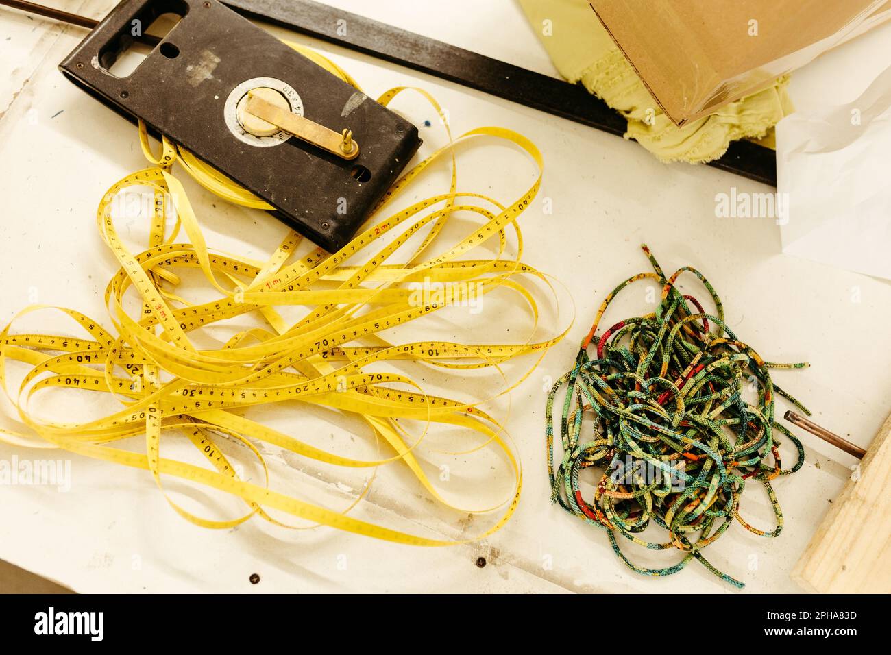 A closeup shot of a yellow measuring tape laying atop a vibrant multi-colored rope, providing a great contrast to the pastel color scheme Stock Photo
