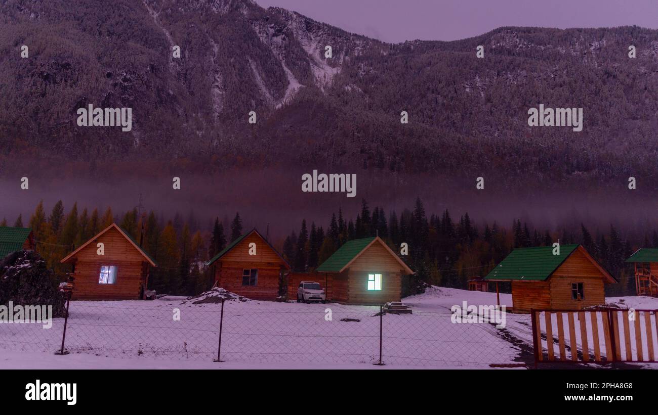 Altai, Russia - October 02, 2022 Auto honda hrv stands by vacation houses with a luminous window near the forest under a mountain with fog and snow at Stock Photo