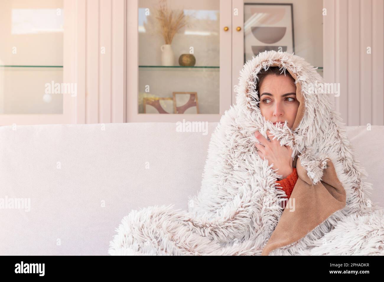 Fatigued female with red running nose and cold fever shivering under warm blanket while relaxing on couch Stock Photo