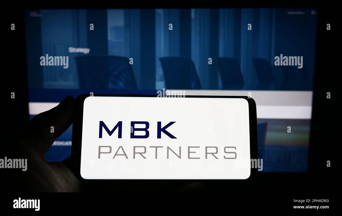 Person holding smartphone with logo of Korean investment company MBK Partners Ltd. on screen in front of website. Focus on phone display. Stock Photo