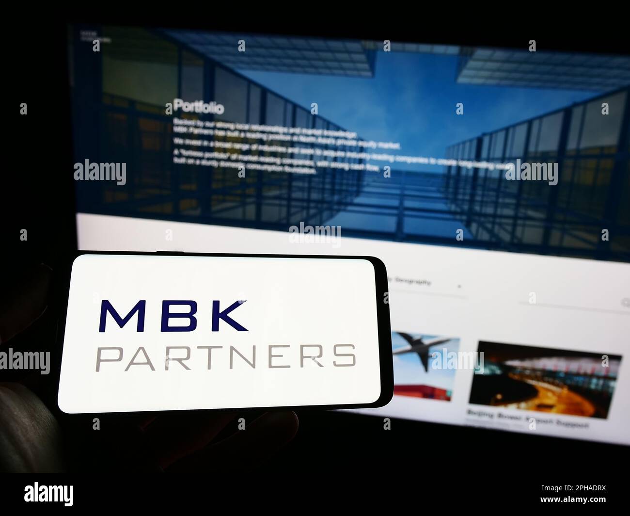 Person holding mobile phone with logo of Korean investment company MBK Partners Ltd. on screen in front of web page. Focus on phone display. Stock Photo