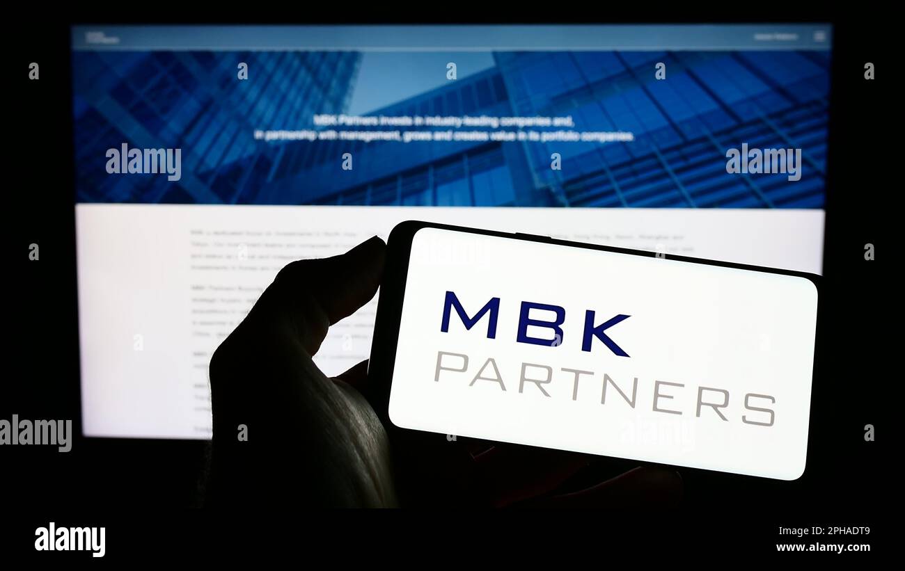 Person holding cellphone with logo of Korean investment company MBK Partners Ltd. on screen in front of business webpage. Focus on phone display. Stock Photo
