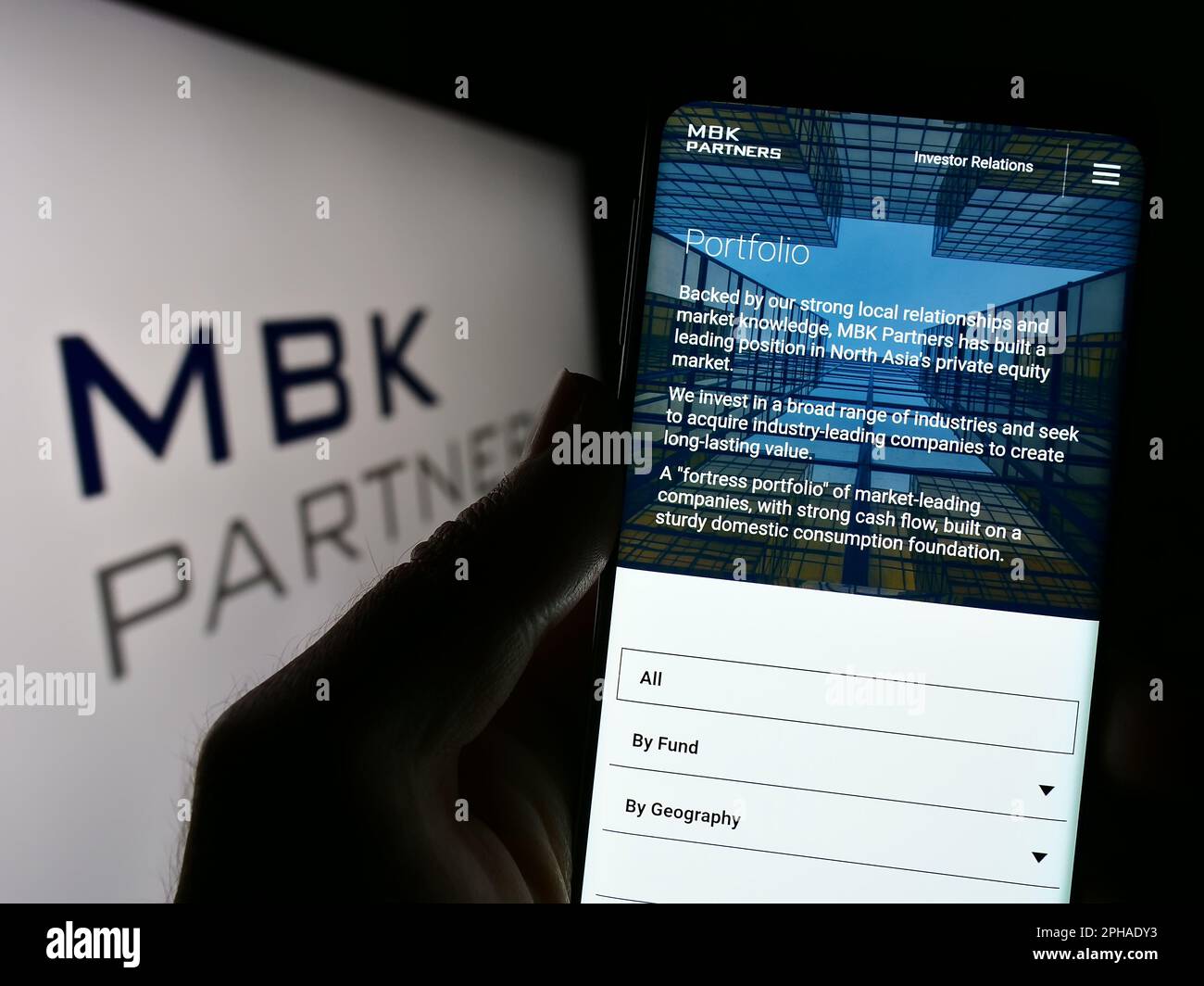 Person holding cellphone with webpage of Korean investment company MBK Partners Ltd. on screen in front of logo. Focus on center of phone display. Stock Photo