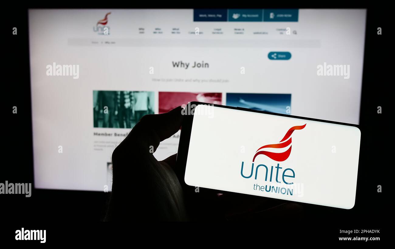 Person holding mobile phone with logo of British trade union Unite the Union on screen in front of web page. Focus on phone display. Stock Photo
