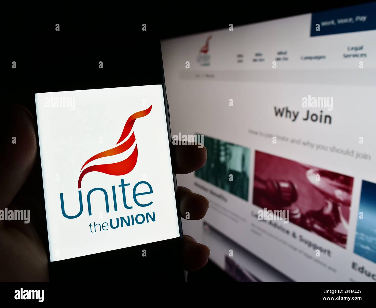 Person holding cellphone with logo of British trade union Unite the Union on screen in front of website. Focus on center of phone display. Stock Photo