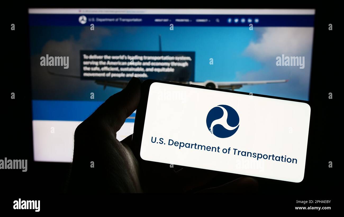 Person holding smartphone with logo of United States Department of Transportation (USDOT) on screen in front of website. Focus on phone display. Stock Photo
