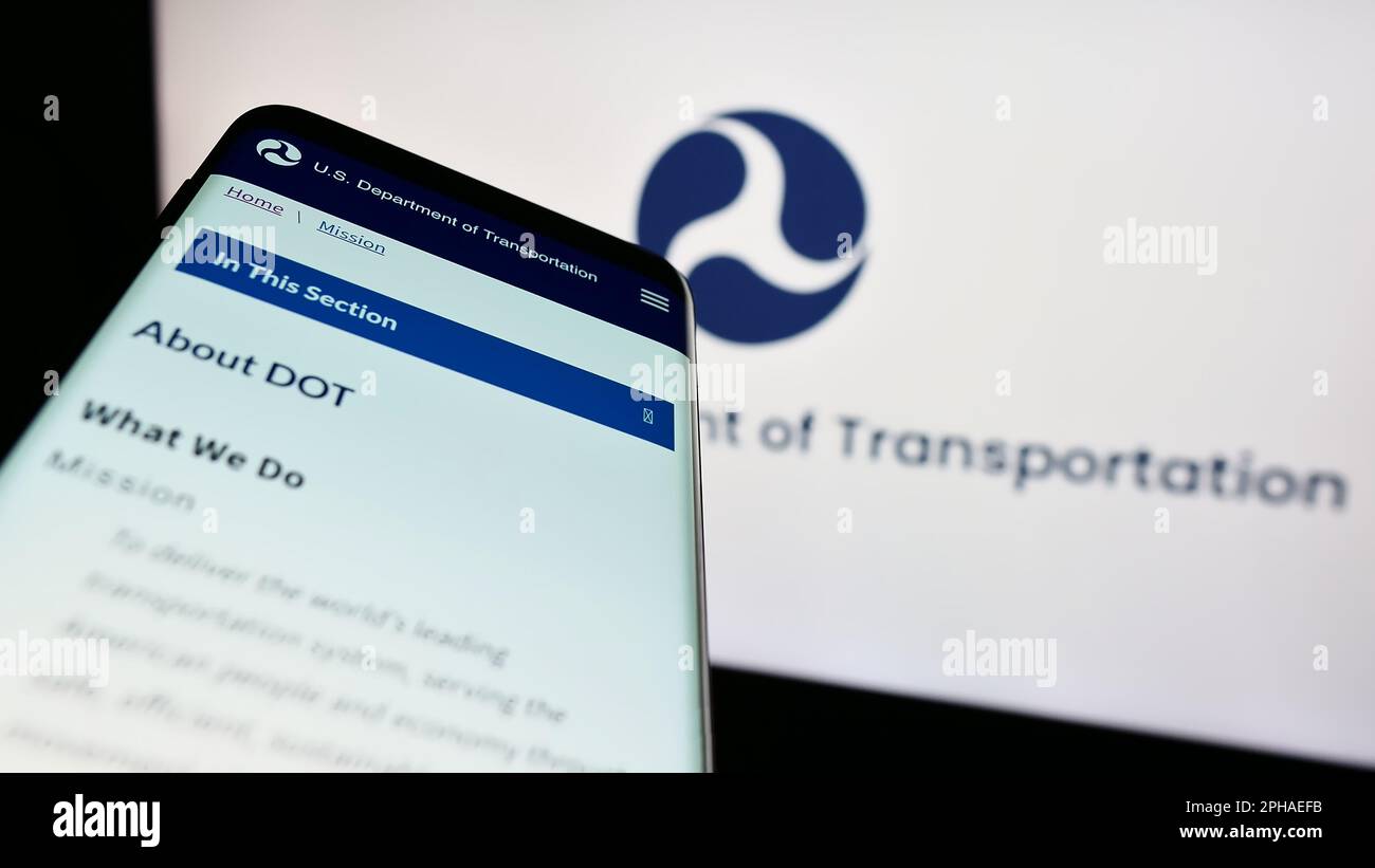 Smartphone with website of United States Department of Transportation (USDOT) on screen in front of logo. Focus on top-left of phone display. Stock Photo