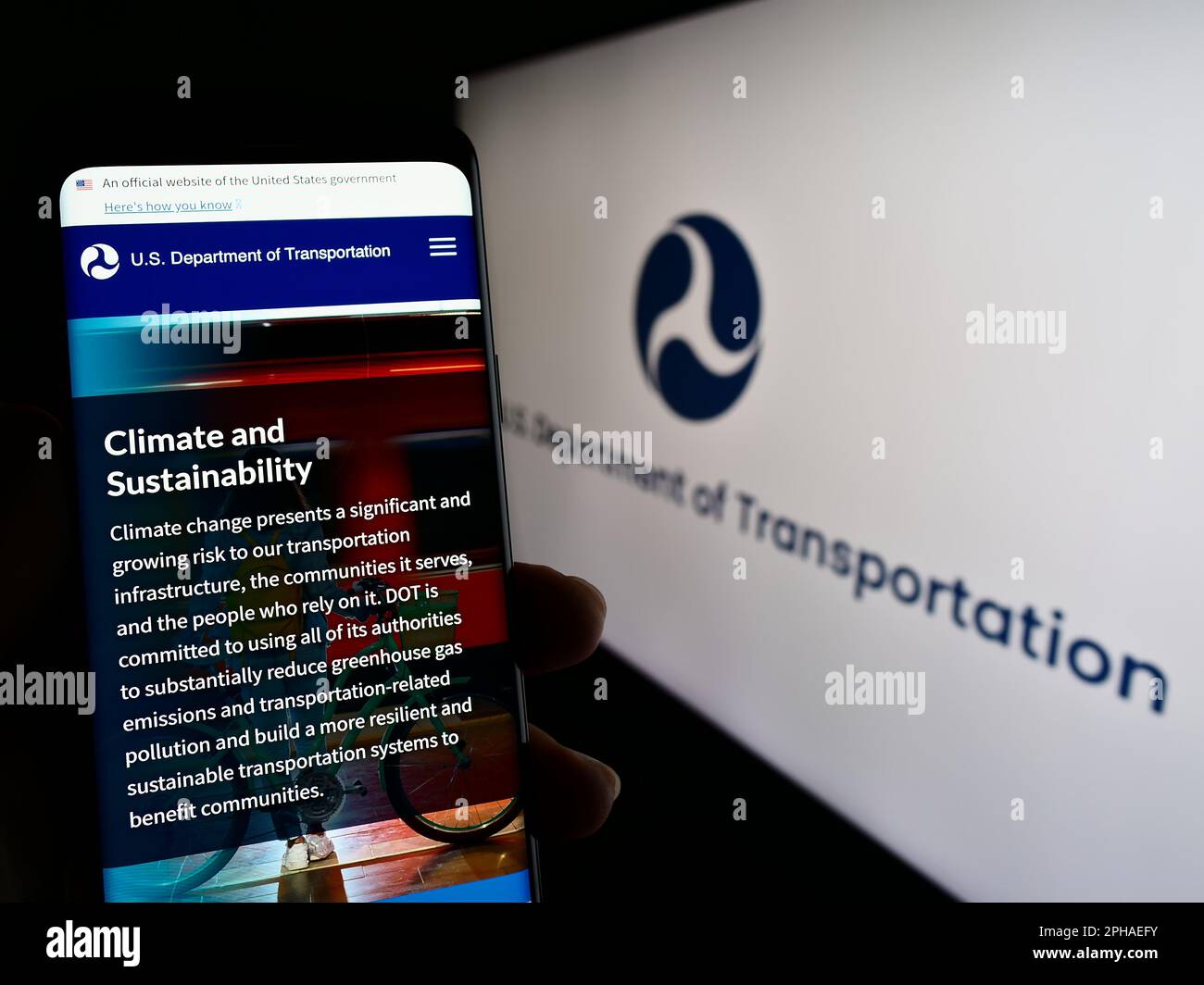 Person holding cellphone with webpage of United States Department of Transportation (USDOT) on screen with logo. Focus on center of phone display. Stock Photo