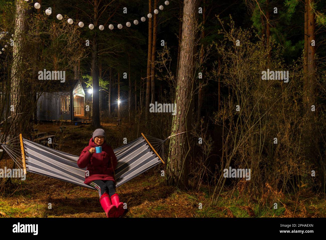Altai, Russia - October 28 2022 A girl in adidas pants sits on a hammock in autumn in a jacket behind vacation houses. Stock Photo
