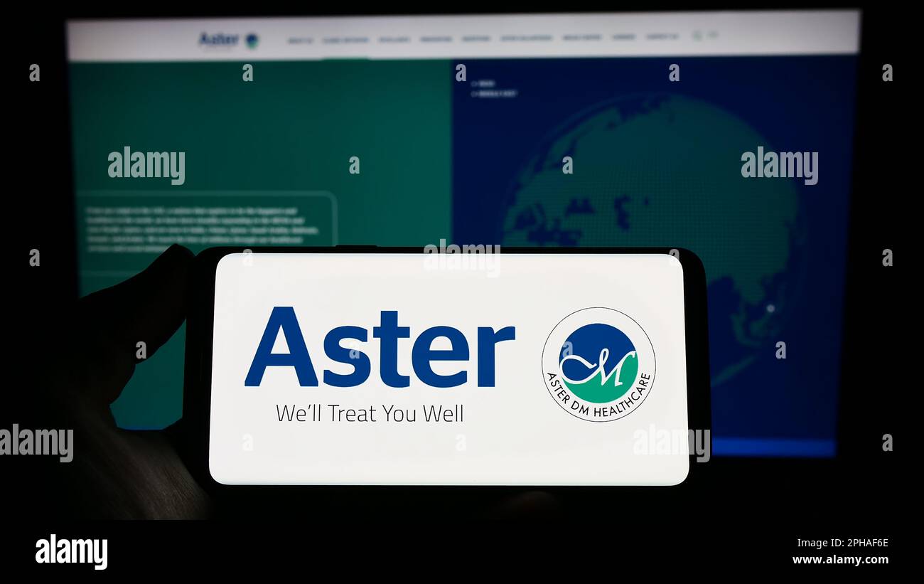 Person holding smartphone with logo of health company Aster DM Healthcare Limited on screen in front of website. Focus on phone display. Stock Photo