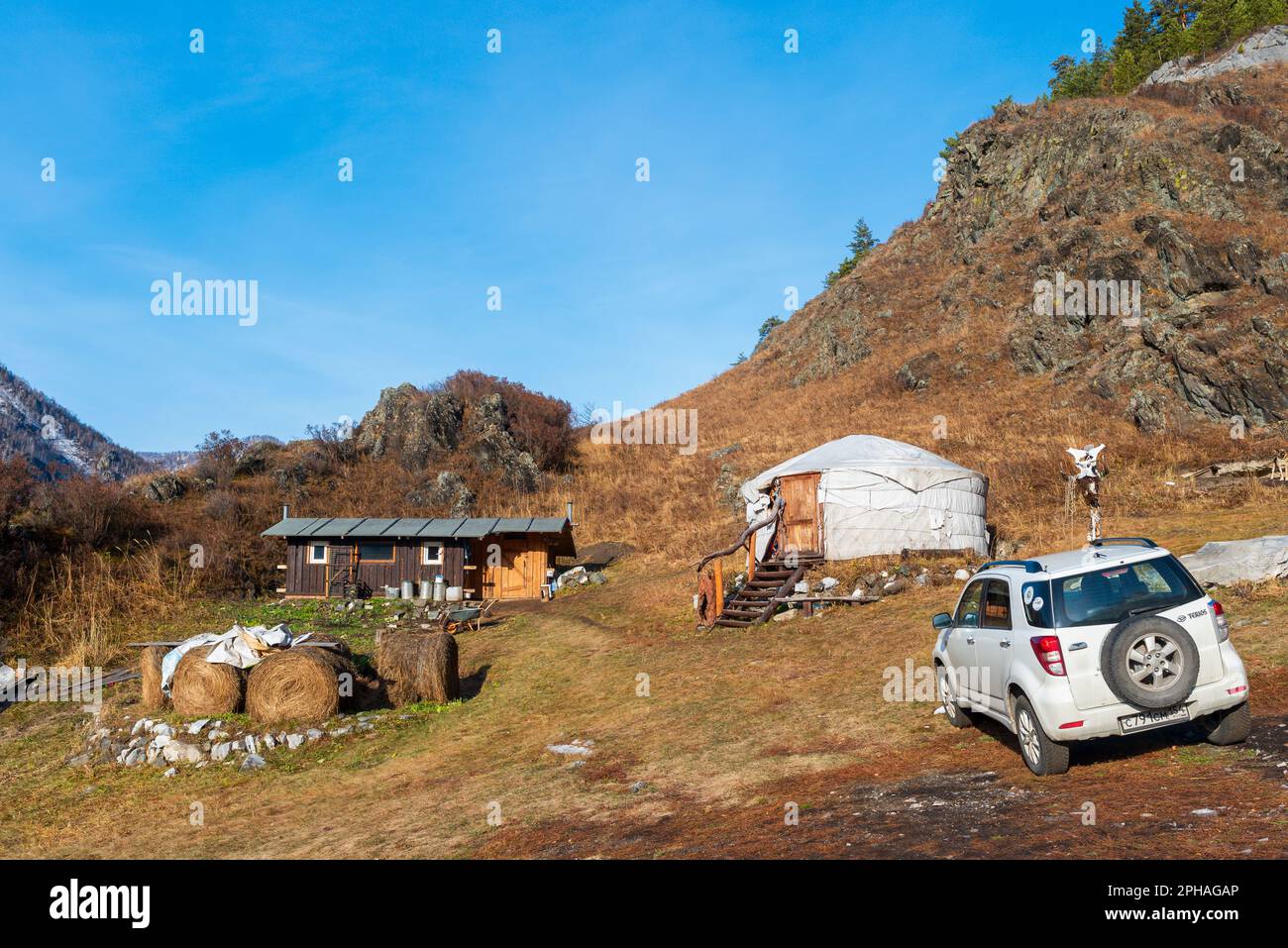 Altai, Russia - October 02, 2022 A Toyota Terios car stands in the mountains with snow next to haystacks and a round house ail in Altai in autumn. Stock Photo