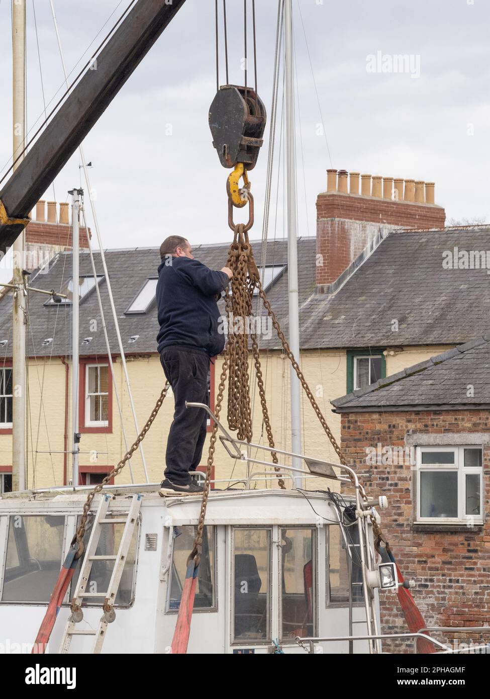 Man adjusts chains prior to lifting a small boat in to the River Nith, Kingholm Quay, Scotland. Stock Photo