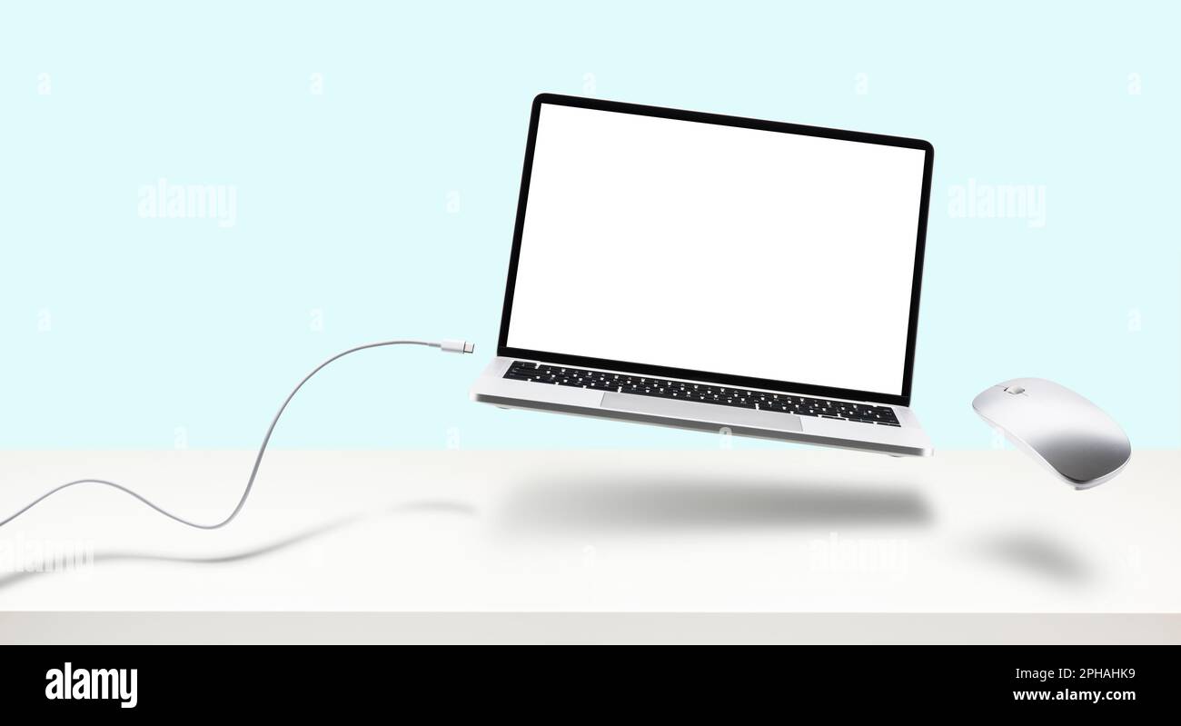 Laptop on white desk with mouse and cable floating. Stock Photo